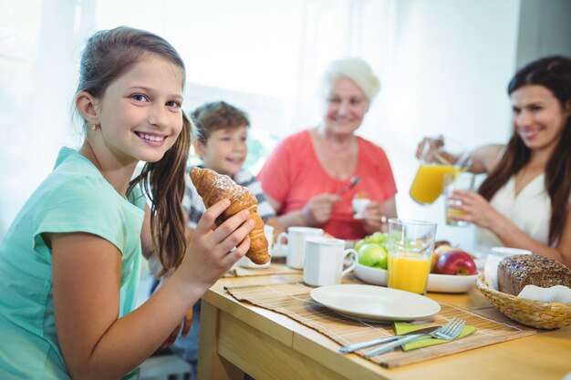 Foto menina sorridente, comer um croissant enquanto tomando café da manhã
