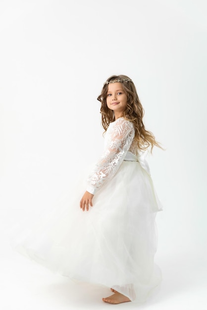 Menina sorridente dançando descalça em um vestido branco em um fundo branco no estúdio