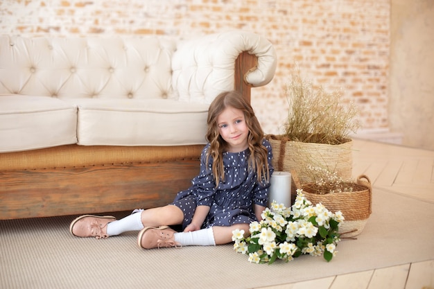 Menina sorridente de cabelo encaracolado com um buquê de flores na sala de estar. Celebração do dia das mães Criança com um buquê de flores para a mãe