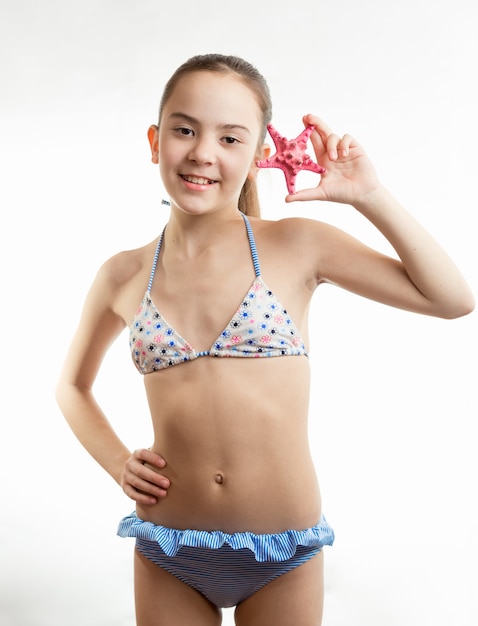 Menina sorridente de maiô segurando estrela do mar vermelha