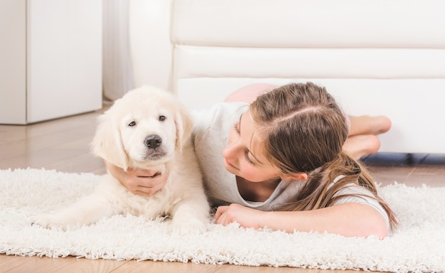 Menina sorridente deitada com o filhote de cachorro retriever fofo e fofo se abraçando no tapete