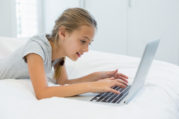 Menina sorridente deitada na cama e usando o laptop no quarto