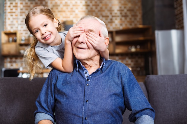 Foto menina sorridente e alegre fechando os olhos do avô enquanto jogava