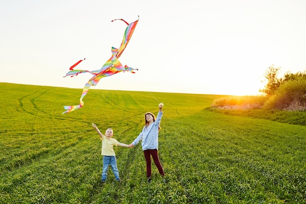 Menina sorridente e irmão menino de pé e de mãos dadas com pipas coloridas voando no prado de grama alta Momentos felizes da infância