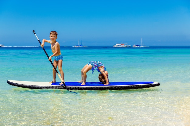 Menina sorridente e menino se divertindo em um paddleboard no mar tropical