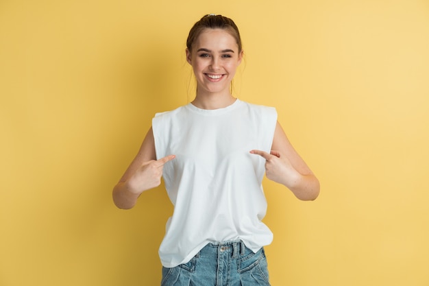 Menina sorridente e positiva aponta os dedos para sua camiseta branca e em branco.