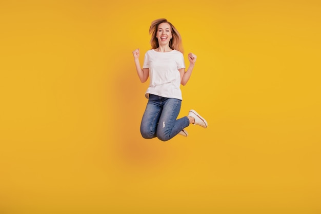 Menina sorridente e positiva pulando no fundo amarelo levantando os punhos celebrando a vitória