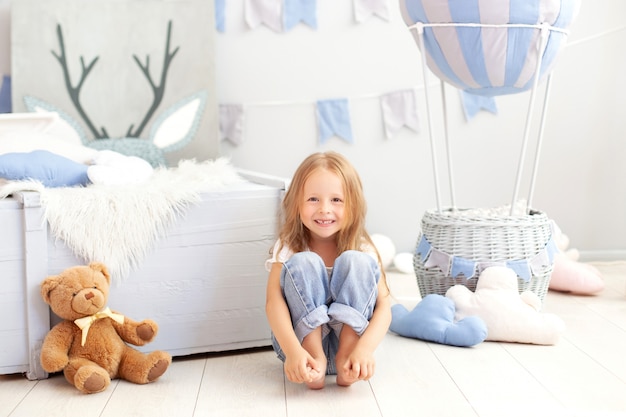 Menina sorridente em jeans senta-se no chão com um balão decorativo. A criança brinca no quarto das crianças.