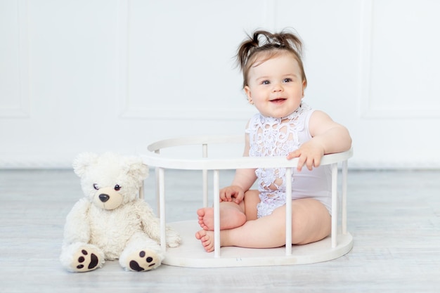 Menina sorridente em uma roupa branca sobre um fundo claro com um ursinho de pelúcia