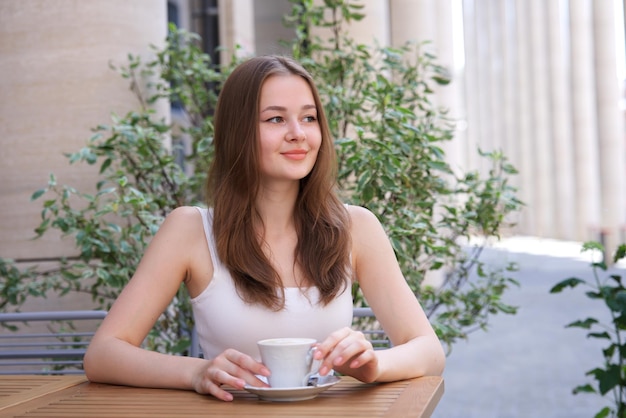menina sorridente feliz jovem sentada ao ar livre no terraço no café bebendo chá ou café