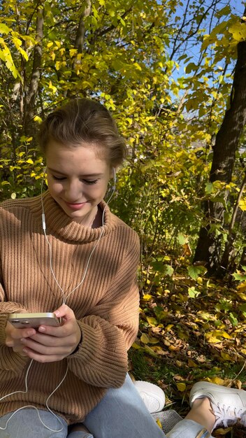 Foto menina sorridente, fones de ouvido, camisola bege da floresta.