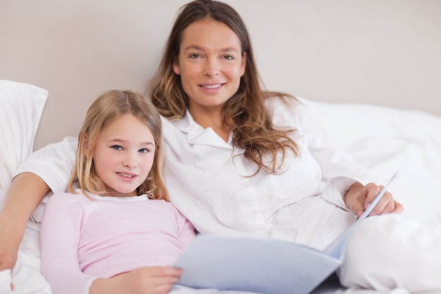 Menina sorridente lendo um livro com sua mãe