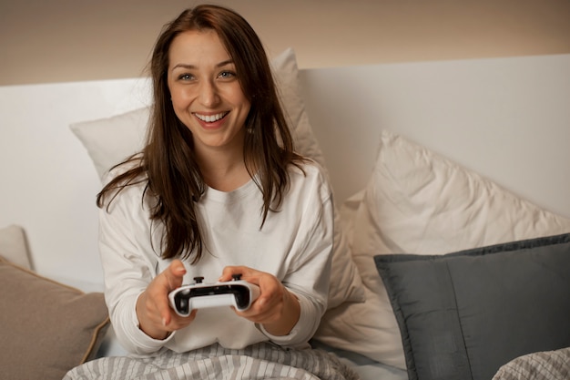 Menina sorridente na cama joga no console e mantém o joystick nas mãos