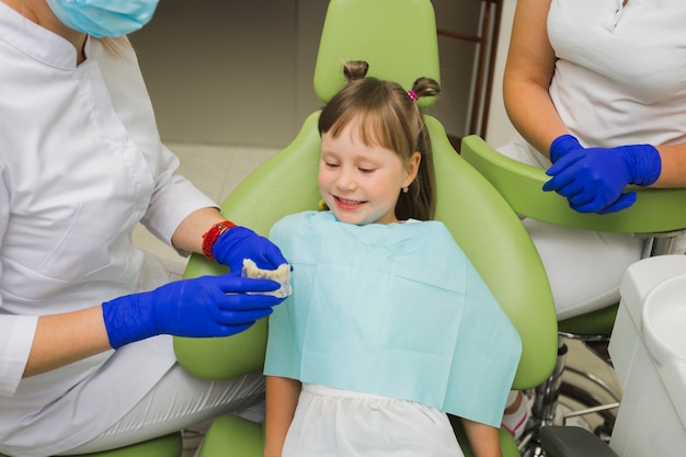 Foto menina sorridente no dentista olhando para dentaduras