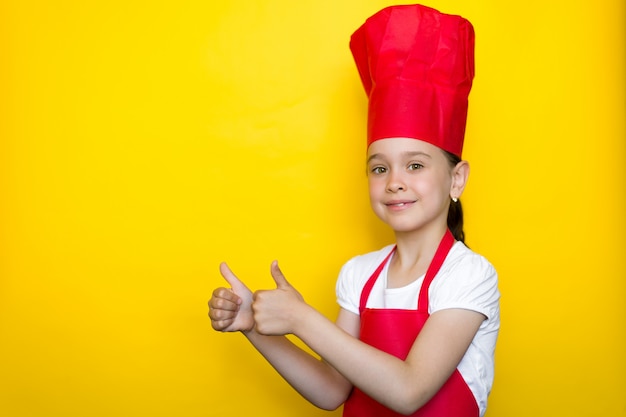 Menina sorridente no terno de um chef vermelho e mostrando o polegar para cima gesto em amarelo