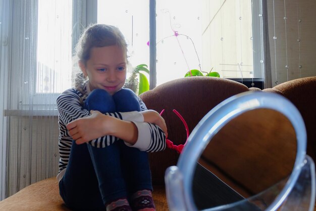 Foto menina sorridente olhando para o espelho enquanto está sentada no sofá