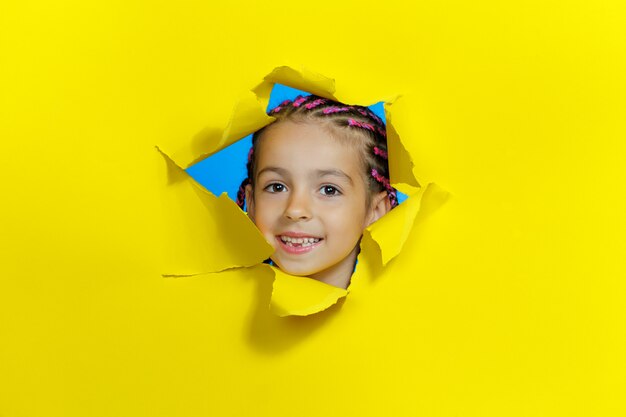 Menina sorridente, olhando por um buraco em um papel amarelo. visualização horizontal. copie o espaço.