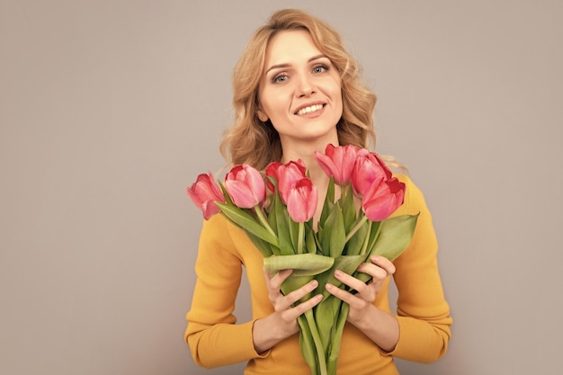 Menina sorridente segura flores para as férias de primavera em fundo cinza