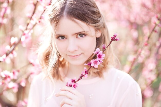 Menina sorridente segurando flores em um pomar de pêssegos