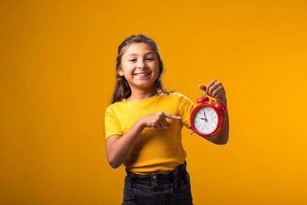 Foto menina sorridente segurando um despertador na mão e apontando o dedo para ele o conceito de educação escola prazos de tempo para estudar