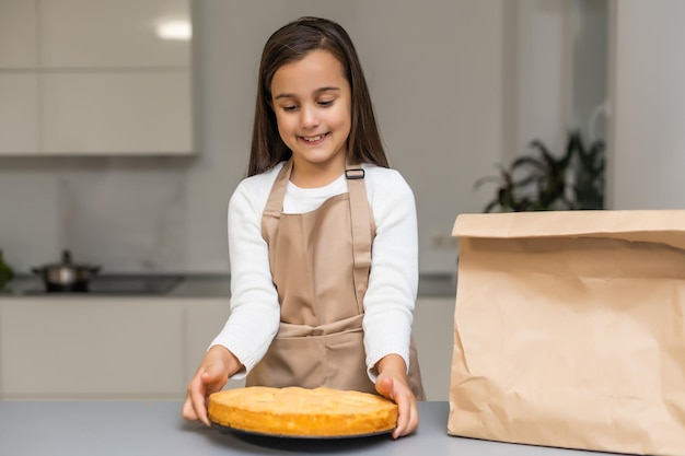 Menina sorridente segurando uma caixa com biscoitos caseiros decorados na cozinha. Presente, pequena empresa, conceito de entrega de doces