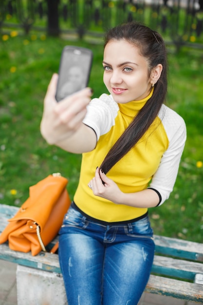 Foto menina sorridente tirando foto com a câmera do smartphone ao ar livre. selfie