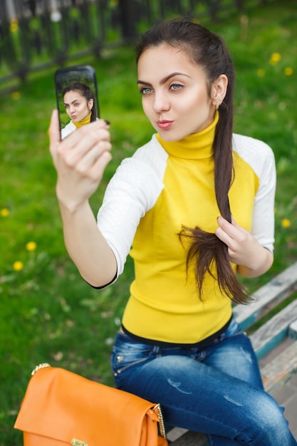 Menina sorridente tirando foto com a câmera do smartphone ao ar livre. selfie
