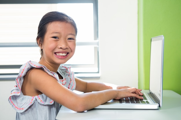 Menina sorridente usando laptop na mesa na sala de aula