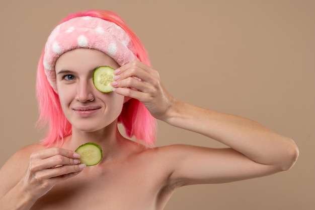 Menina sorridente usando pepino para cuidar do rosto