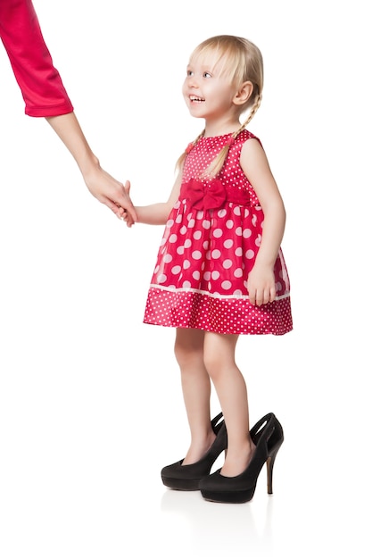 Menina sorridente usando sapatos grandes, matando a mão de sua mãe. Isolado em fundo branco