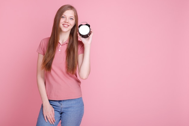 Menina sorrindo com despertador em fundo rosa