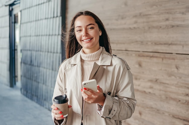 Menina sorrindo e segurando um telefone e uma xícara de café contra o pano de fundo do edifício