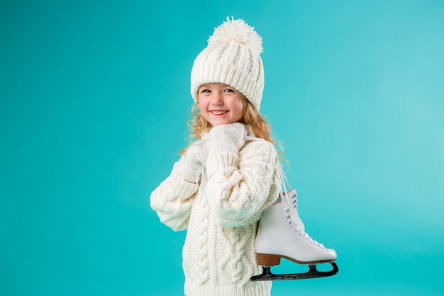 menina sorrindo em um chapéu de inverno branco e blusa, segurando patins