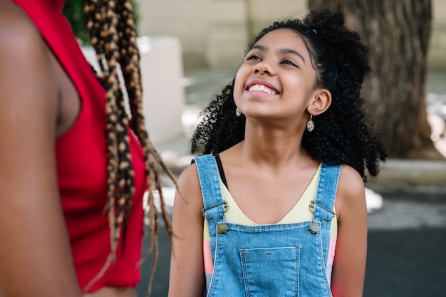 Menina sorrindo enquanto desfruta de um passeio com a mãe ao ar livre na rua.