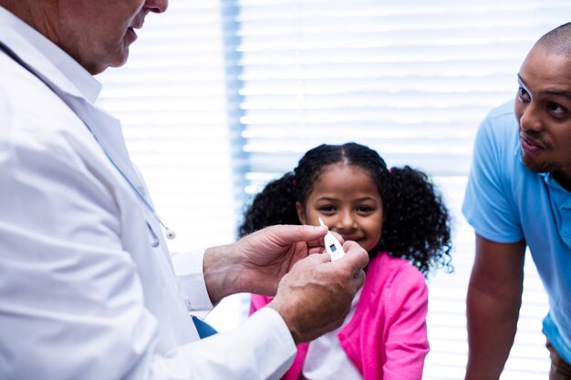 Menina sorrindo enquanto médico verificar temperatura no termômetro