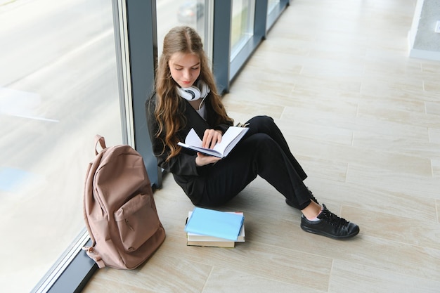 Menina sorrindo Linda colegial sorrindo enquanto está sentado perto da janela e lendo o livro