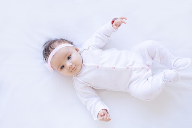 Foto menina sorrindo na cama em um fundo branco isolado em uma cama de algodão adormecendo ou acordando de manhã bebê recém-nascido fofo em casa closeup