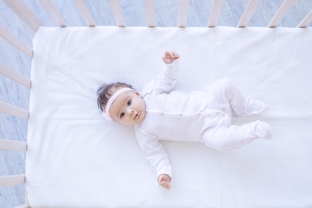 Foto menina sorrindo na cama em uma cama de algodão branco adormecendo ou acordando de manhã lindo bebê recém-nascido em casa no berço closeup