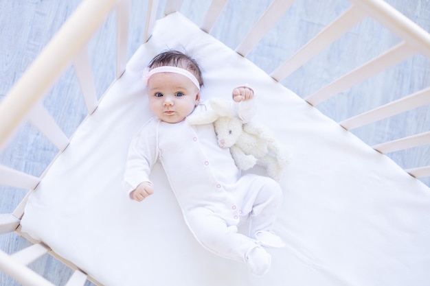 Menina sorrindo na cama em uma cama de algodão branco com um brinquedo adormecendo ou acordando de manhã bebezinho fofo em casa