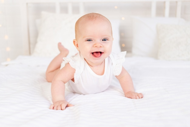 Menina sorrindo ou rindo deitada de bruços em uma cama de algodão branco em casa