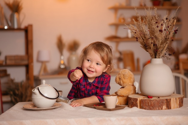 Menina sorrindo tomando café da manhã na cozinha com um ursinho de pelúcia