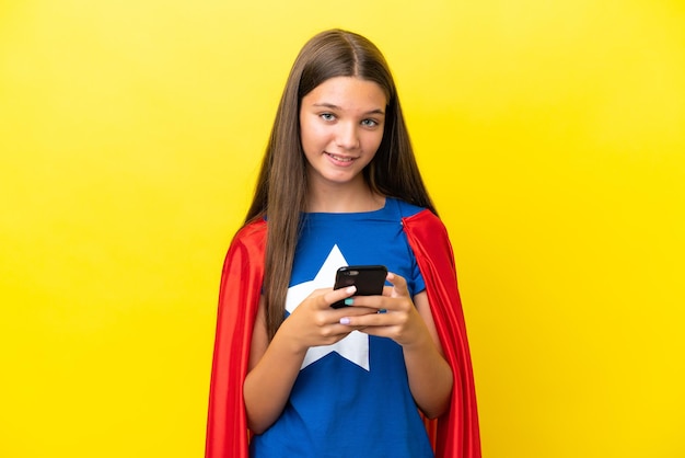 Menina super-heroína caucasiana isolada em fundo amarelo enviando uma mensagem com o celular