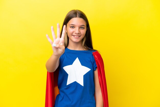 Menina super-heroína caucasiana isolada em fundo amarelo feliz e contando quatro com os dedos