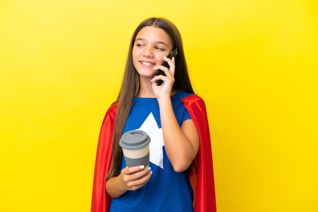 Menina super-heroína caucasiana isolada em um fundo amarelo segurando um café para levar e um celular