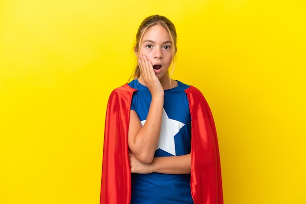 Menina super-heroína isolada em um fundo amarelo surpresa e chocada ao olhar para a direita