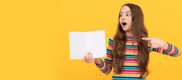 Menina surpreendida aponta o dedo para o livro aberto para espaço de cópia fundo amarelo apontando Banner de estudante estudante Retrato de aluno de escola com espaço de cópia