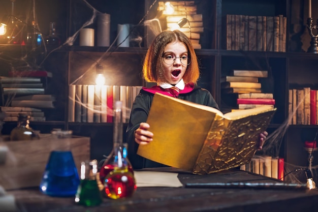 Menina surpresa com fantasia de bruxa segura livro mágico de festa de Halloween Cosplay