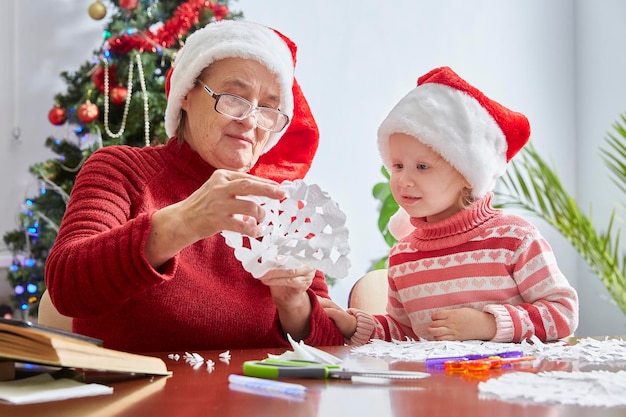 Menina surpresa olha para o artesanato da avó para o ano novo e o Natal. Chapéu de Papai Noel como um símbolo do Natal.