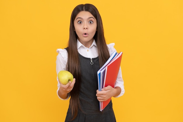 Menina surpresa segura fundo amarelo de livros didáticos de maçã e escola, lição de casa.