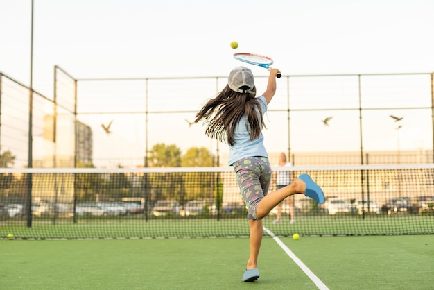 Menina tentando jogar tênis na quadra ao ar livre